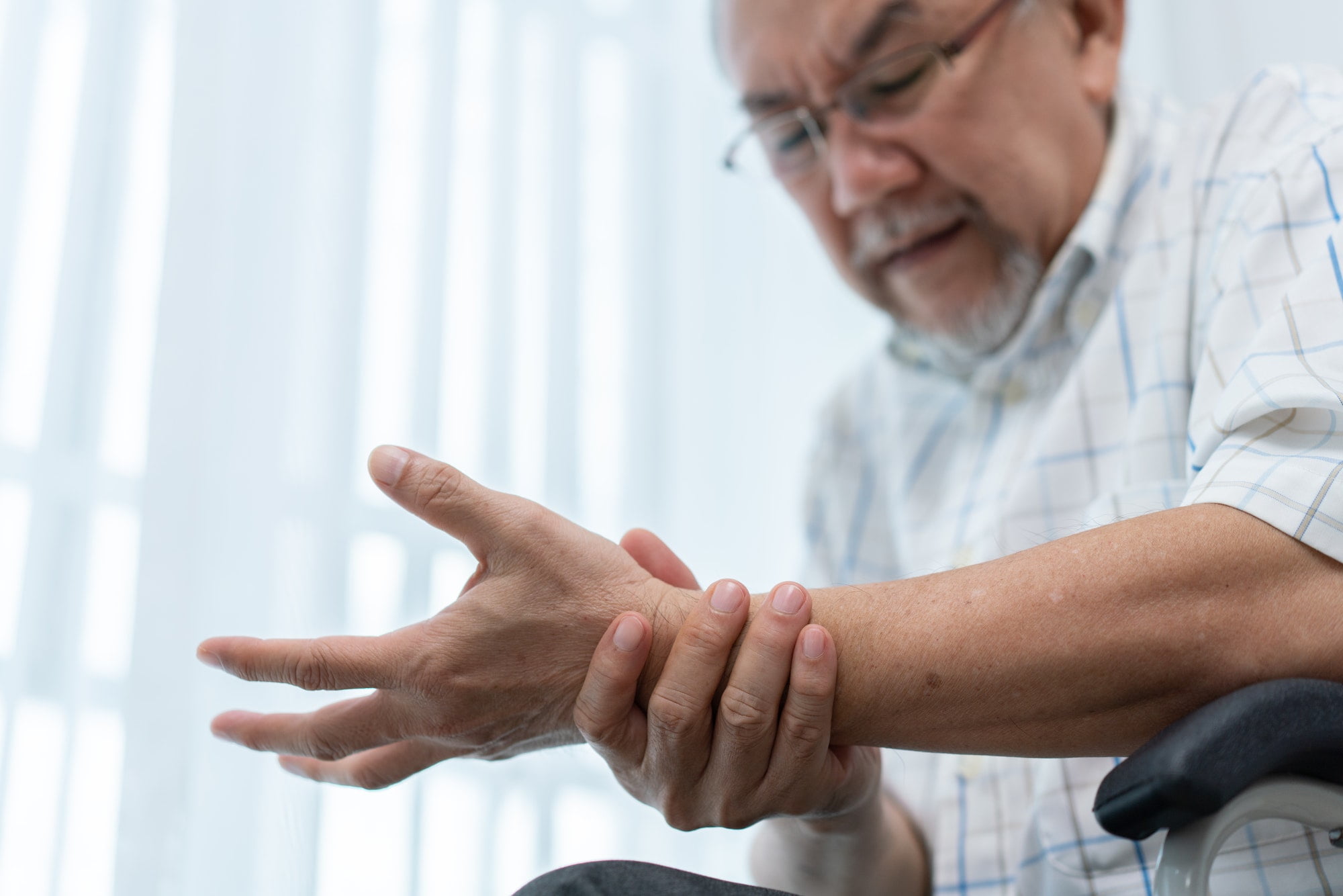 Senior man massaging wrist and arm to relieve suffering from joint pain