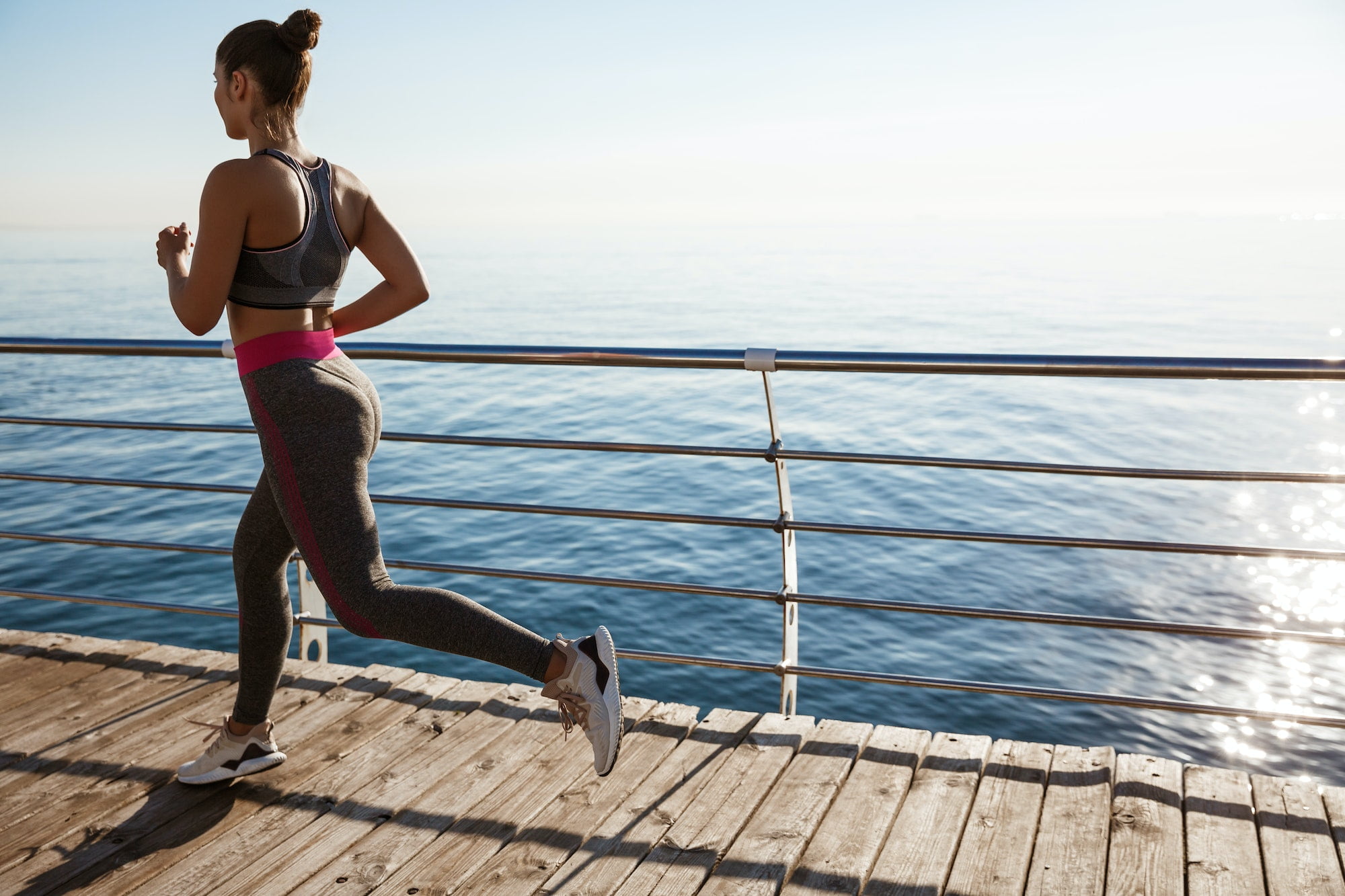 Rear view of female athlete workout on the seaside promenade, jogging near sea