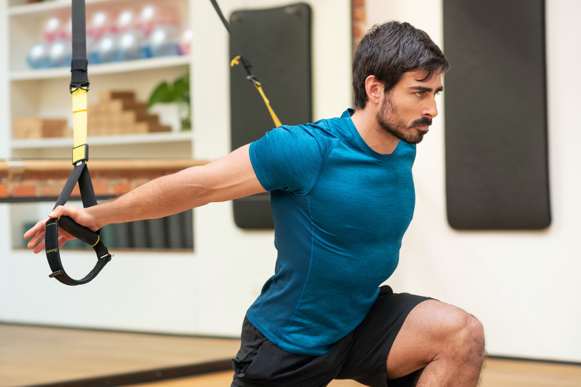 Muscular sportsman stretching shoulders on TRX straps